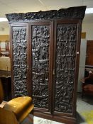 A profusely carved Chinese decorated dark wood three-section wardrobe