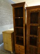 A modern hardwood tall narrow open shelving unit with three drawers to the base