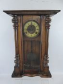 An Antique Wooden Wall Clock, with columns to either side, Roman numerals on cream enamel face,
