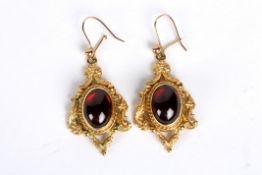 A pair of Victorian style cabochon garnet set drop earrings the central oval garnets within