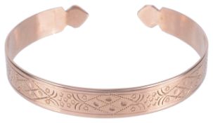 An early 20th century scroll engraved open banglethe rose coloured metal with floral and scroll