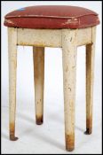 A vintage mid 20th century industrial stool raised on a shaped metal frame with a red vinyl seat