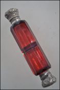 A Victorian facet cut cranberry glass double ended perfume bottle with unmarked rococo silver