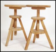 A pair of solid wood retro artists stools having adjustable height seat pads raised on tripod