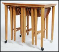 A vintage mid 20th century teak side - nest of tables with a trio of slide out metamorphic round