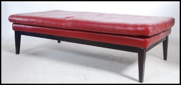 A contemporary large red leather ottoman footstool of rectangular form having ebonised tapered leg