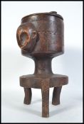 An unusual African tribal art foot pot on stand having figural face mask handles,raised on chased