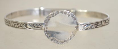 A silver adjustable bangle bracelet having hand worked roundel to front and inset leaf pattern.