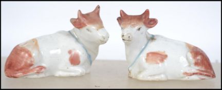A pair of 19th century Staffordshire cow figurines. Each being seated having bells to neck.