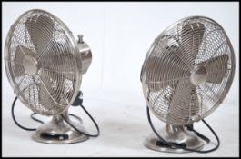 A pair of retro style 20th century metal wire work electric fans raised on a pedestal base. Measures