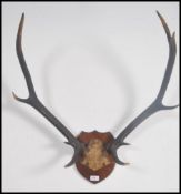 A good set of mounted Stag antlers set to an armorial mahogany plaque having partially legible