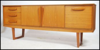 A 1970's Danish inspired teak sideboard having a low and wide body with angular supports. The body