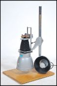 A mid century Industrial photograph enlarger by Universal alpha being raised on a wooden plinth