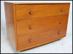 A 20th century Ercol windsor pattern elm chest of drawers being raised on ball castors with flared
