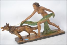 An art Deco chalk ware figurine of a stylish lady walking an Alsatian dog on a blustery day raised