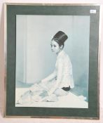 A mid century retro mounted print of a Malaysian girl in robes being signed by the artist with