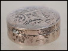 A silver pill box with chase decorated lid. Marked