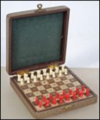 A vintage mid century travelling chess set with white and red pieces in hinged top travel case