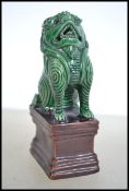 An unusual Chinese figurine of a green glaze temple dog / fu dog being raised on a brown glazed