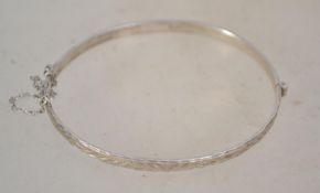 A hallmarked silver bangle bracelet having a half engraved design and safety chain. Weighs 8.1 grams