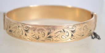 A 9 carat cold metal core bangle bracelet with safety chain having half engraved foliate design,
