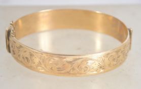 A 9 carat gold metal core bangle bracelet with safety chain having half engraved foliate design,