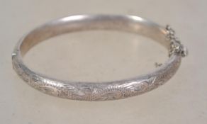 A silver hallmarked bangle bracelet having a half engraved foliate swirl design with safety chain.