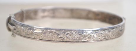 A hallmarked silver bangle bracelet, having half engraved foliate design with safety chain.