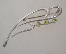 A sterling silver 925 brooch having a wave design with three peridot stones with rollover catch.