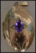 A hallmarked 9ct gold locket set with an oval cut amethyst having etched decoration. Hallmarked