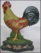 A vintage style painted cast iron doorstop in the form of a cockerel facing left raised on a