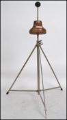 A vintage early 20th century wig stand raised on an adjustable tubular metal tripod base with wooden
