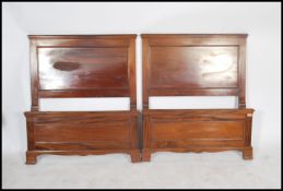 A pair of Edwardian mahogany single beds having panelled head and footboards being united by the bed