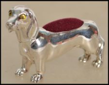 A large silver pin cushion in the form of a dog - dachshund hainv red baize lined cushion atop.