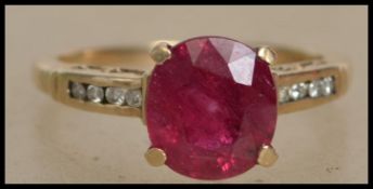 A hallmarked 9ct gold ring set with a central ruby with diamond accent shoulders. Hallmarked