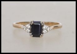 A hallmarked 9ct gold ring set with a central emerald cut sapphire with white stone accents .