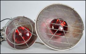 Two vintage 20th century retro industrial heat lamps of grey metal construction having wire cages to