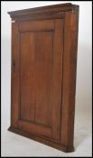 A 19th century Georgian country oak corner cupboard having plinth base and shaped top with central