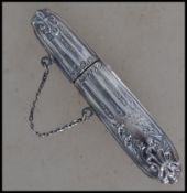 A rococo silver embossed ladies needle case of cylindrical form with safety / chatelaine chain.