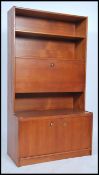 A 1970's retro teak wood upright bookcase having shaped shelves over fall front cabinet and cupboard