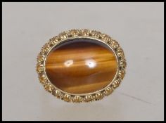 A hallmarked 9ct gold ring set with a large oval tigers eye stone surrounded by a yellow stone halo.