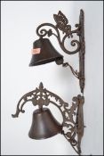 Two vintage style cast iron bells having wall mounted brackets, both having rococo leaf and swirl