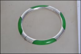 A vibrant green jade bangle held in a 925 silver bangle etched with light detailing having a snap