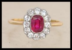 An 18ct gold, platinum ruby and diamond cluster ring. The central ruby being oval cut with diamond