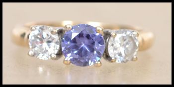 A 9ct gold three stone ring set with a central purple round cut stone flanked by two white stones.