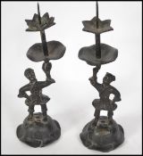 A pair of 19th century Oriental bronze candlesticks in the form of figure raised on pedestal bases