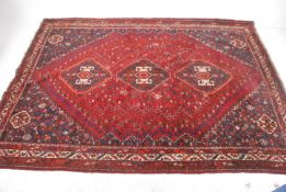 A large Persian floor rug with geometric patterns to the red ground having decorative borders