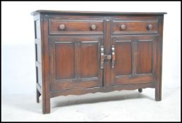 An Ercol dark elm dresser base having a pair of carved panel doors with shelving to the inner raised
