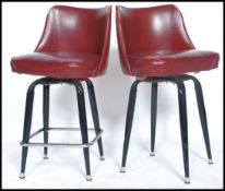 A pair of American vintage style bar stools in red vinyl and piping with shaped backrests and padded