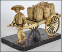 An Oriental faux bone Okimono figurine of a merchant man pulling a cart of resin construction raised